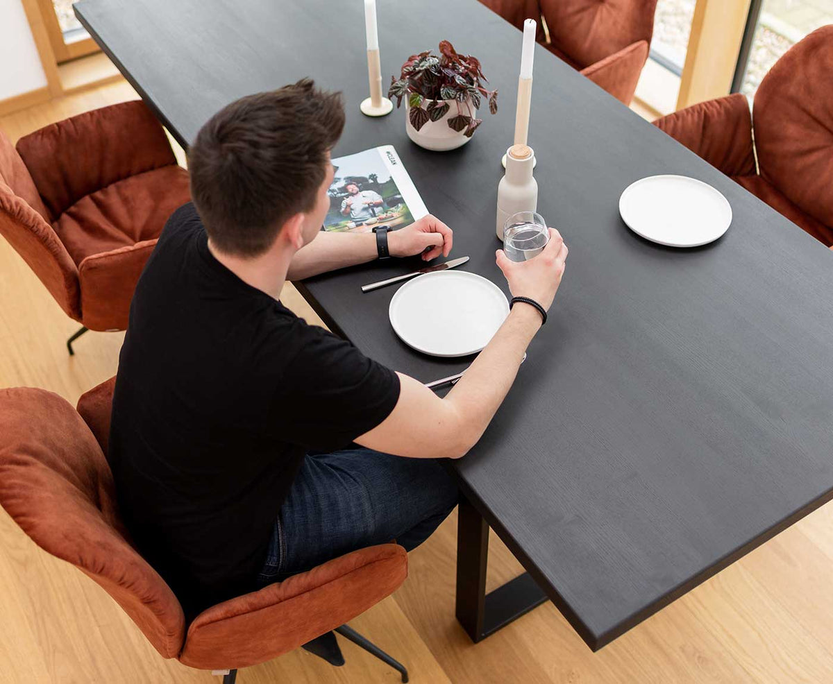 Seitliche Aufnahme von Holz Tischplatte Schwarz mit Gestell und Dekoration und Person beim Trinken.