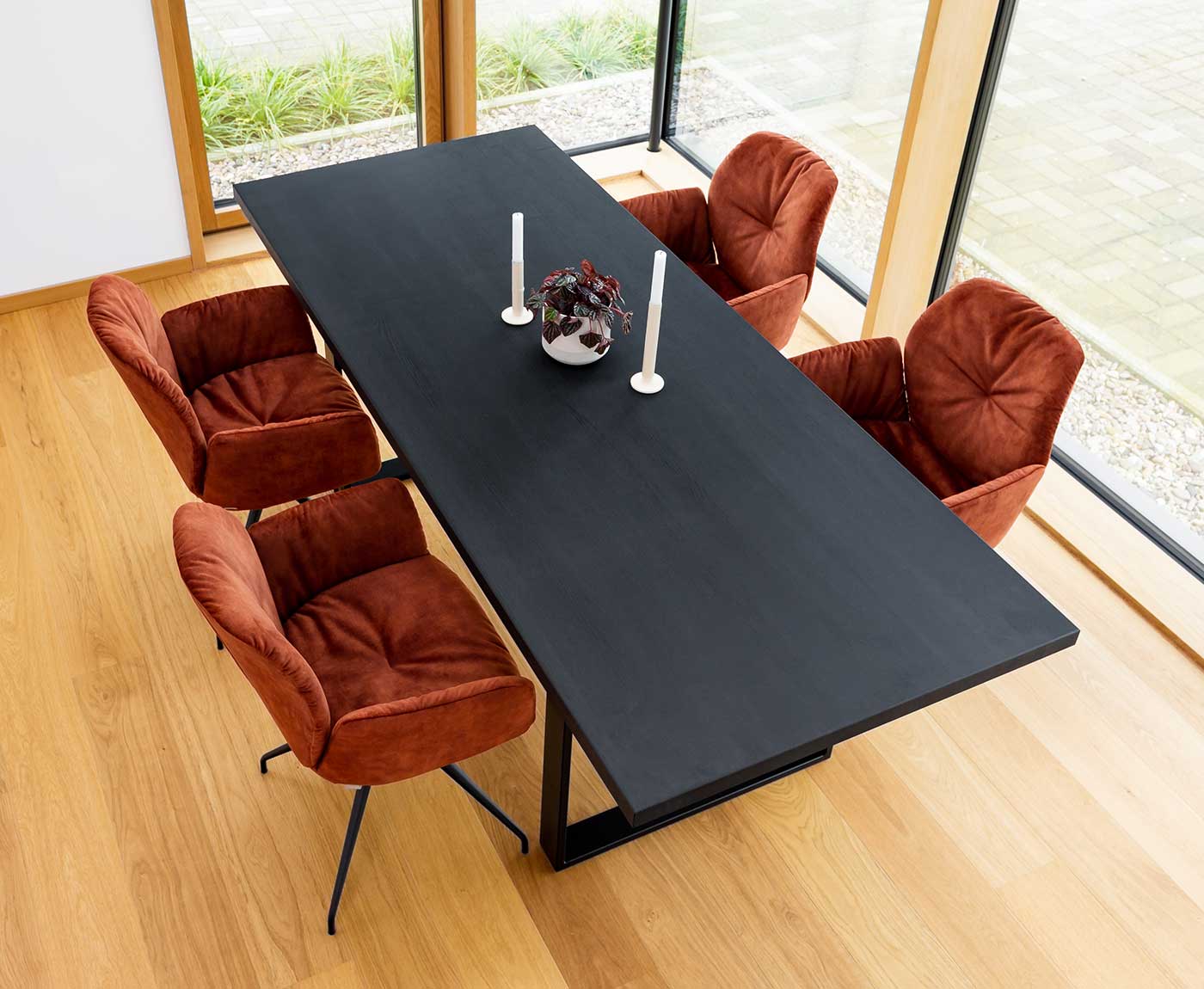 Schwarze Tischplatte aus Holz mit Gestell und vier Stühlen - dekoriert mit Kerzen und Pflanze.