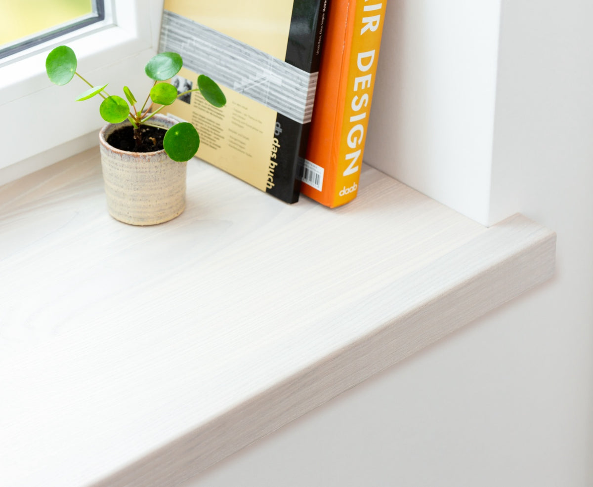 Nahaufnahme einer weißen Aufsatzfensterbank aus Holz, mit Büchern und Pflanze. Aufkantung verdeckt alte Fensterbank. 