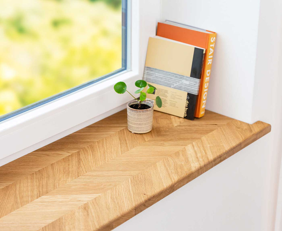 Eckaufnahme der Fensterbank innen in Fischgrät mit Dekoration aus Pflanze und Büchern.