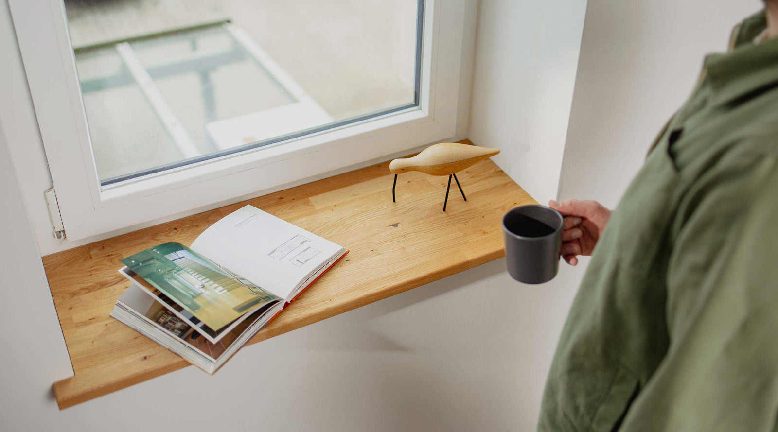 Mann steht an der Fensterbank und trinkt Kaffee