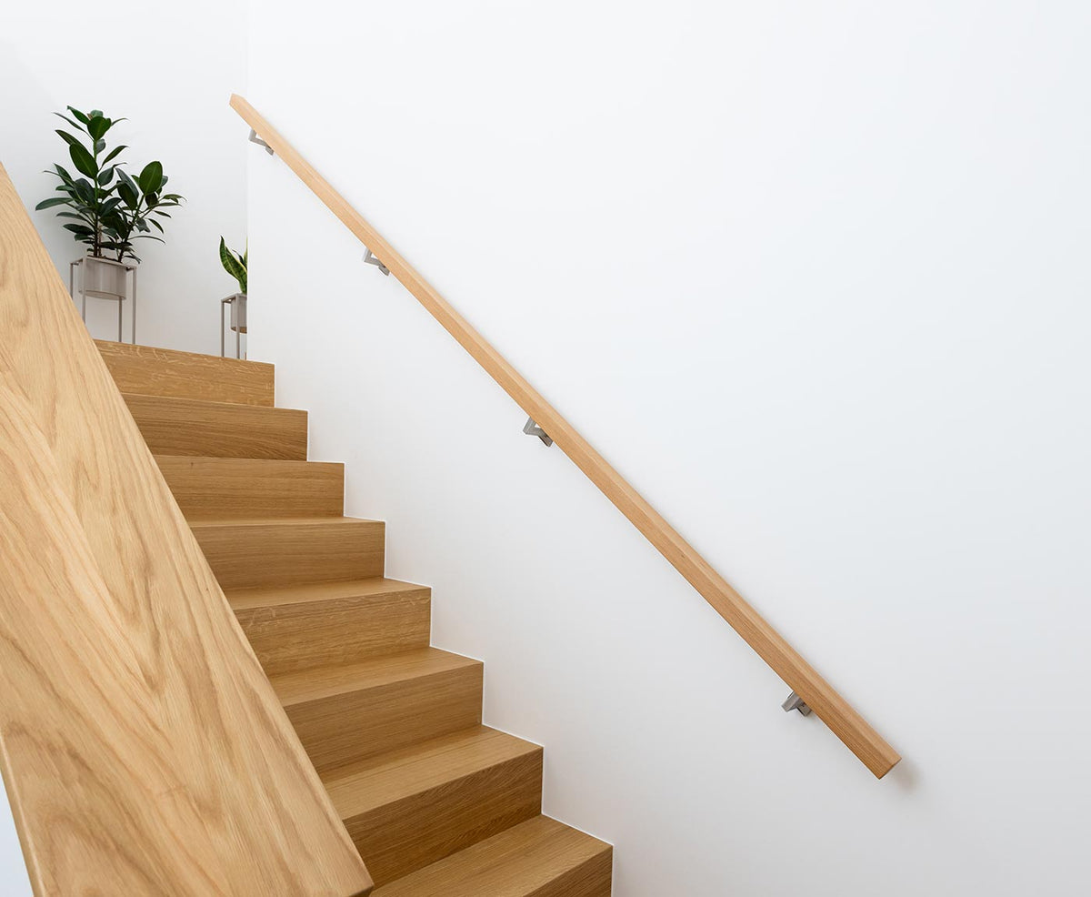 Langer Handlauf Treppe aus Buche, mit Edelstahlhaltern an weißer Wand montiert - passend zur Holztreppe.
