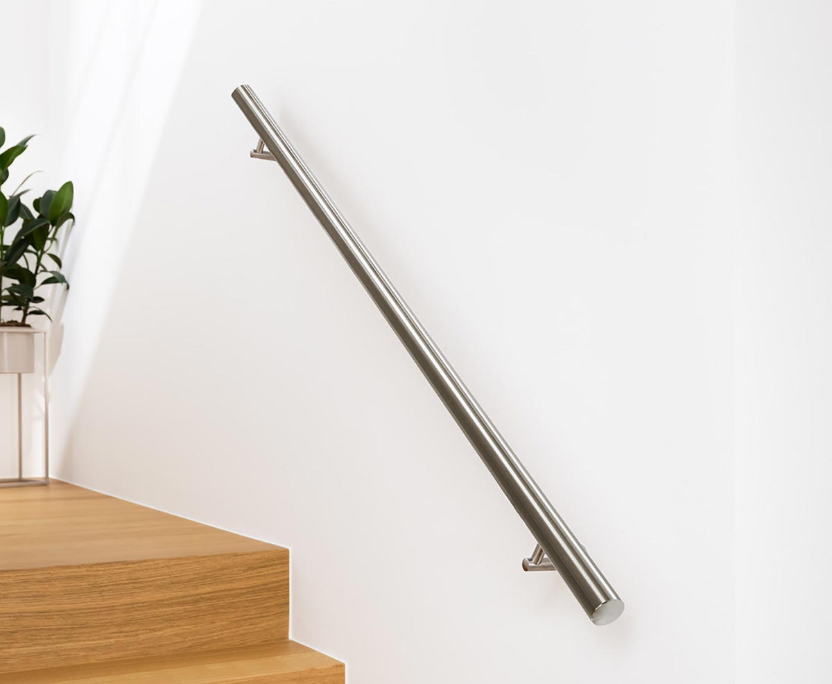 Runder Handlauf Edelstahl mit passenden Haltern an weißer Wand über Holztreppe montiert.