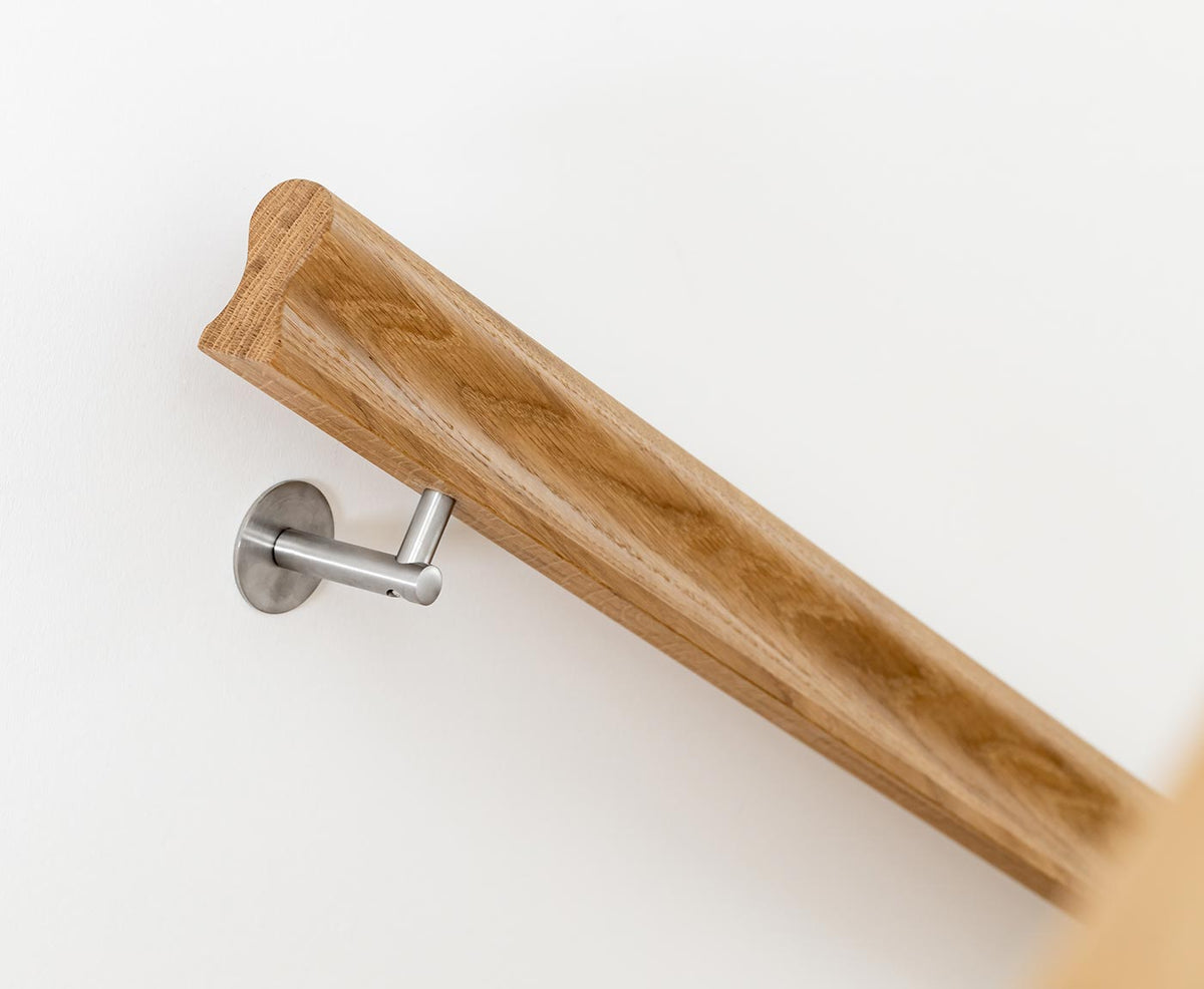 Nahaufnahme eines omega Handlaufs aus Eiche, mit klassischem Edelstahlhalter an weißer Wand.