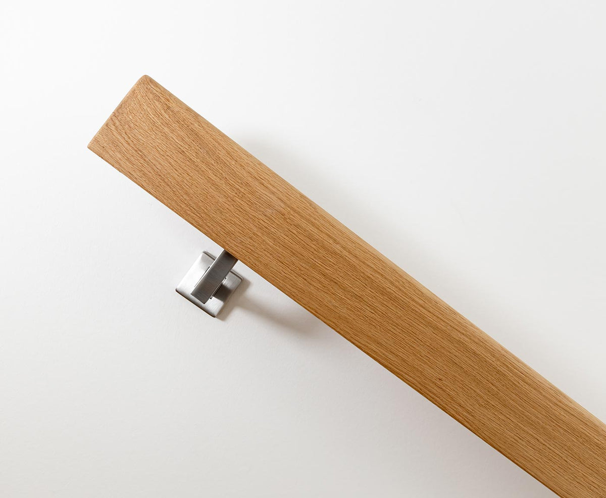 Seitenansicht eines Handlaufs aus Eiche, mit Edelstahl-Handlaufhalter an weißer Wand montiert.
