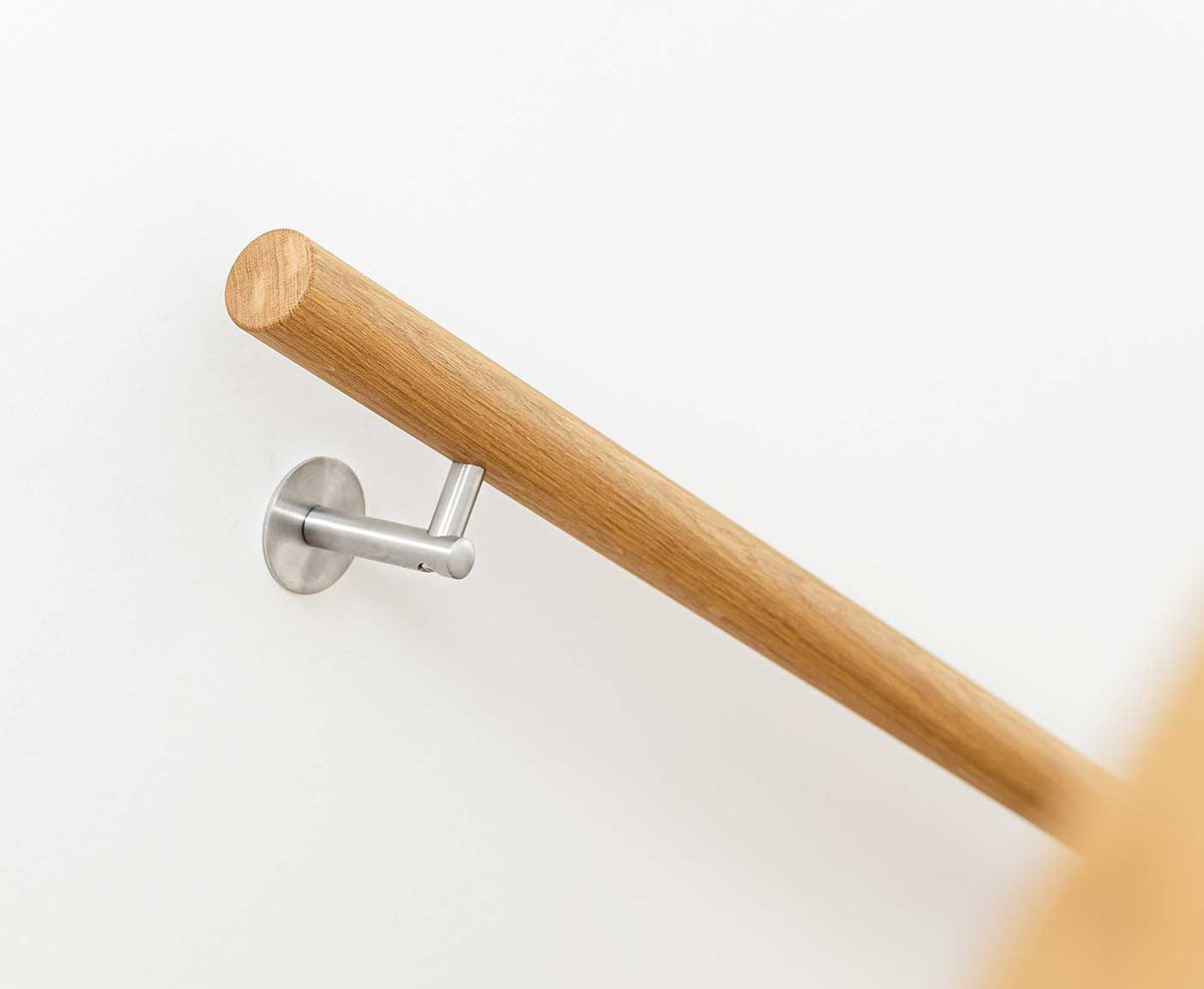 Handlauf rund aus Eiche mit Edelstahlhalter an weißer Wand.