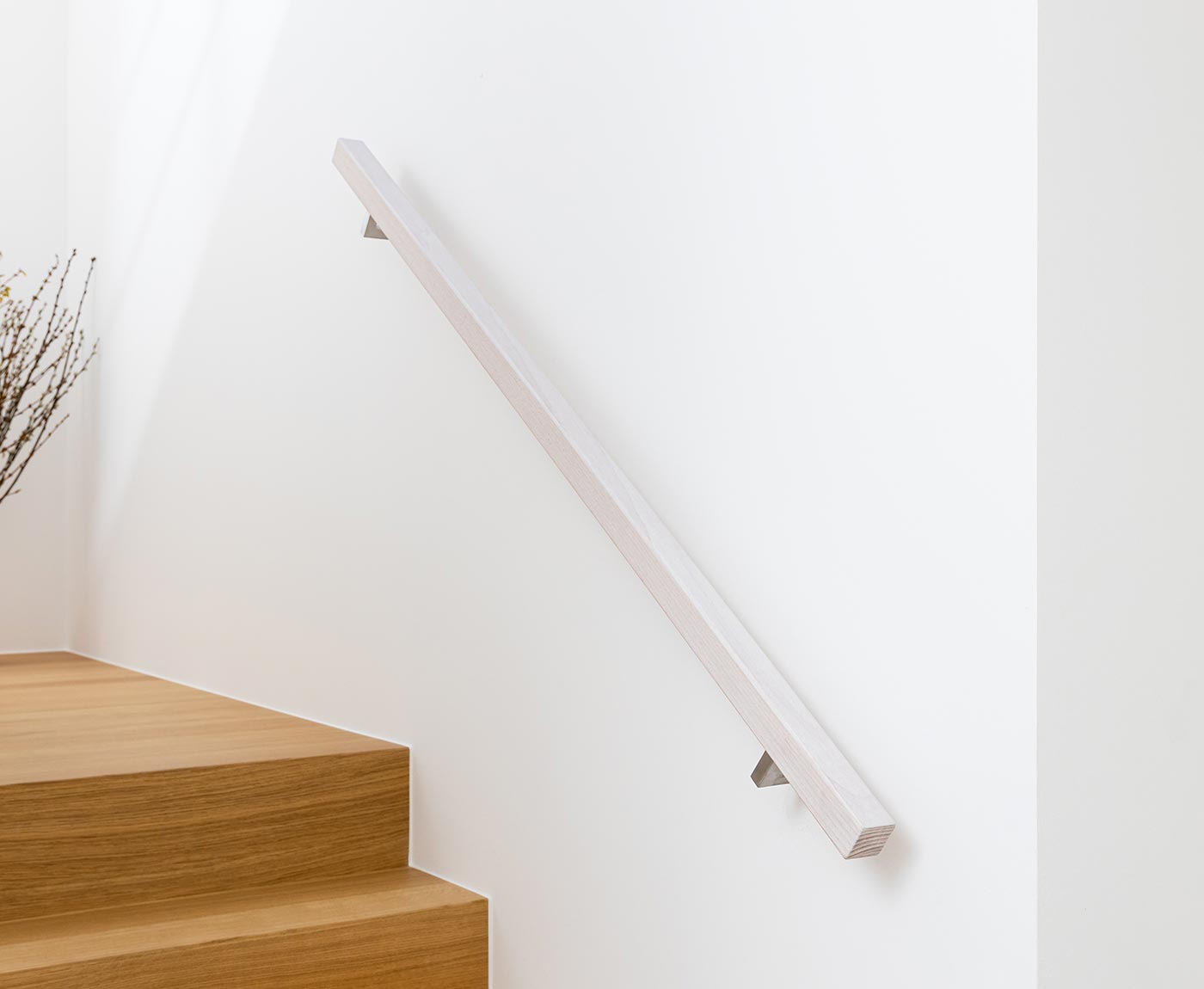 Quadratischer, weißer Handlauf aus Holz an weißer Wand - als Treppengeländer innen über Holztreppe montiert.