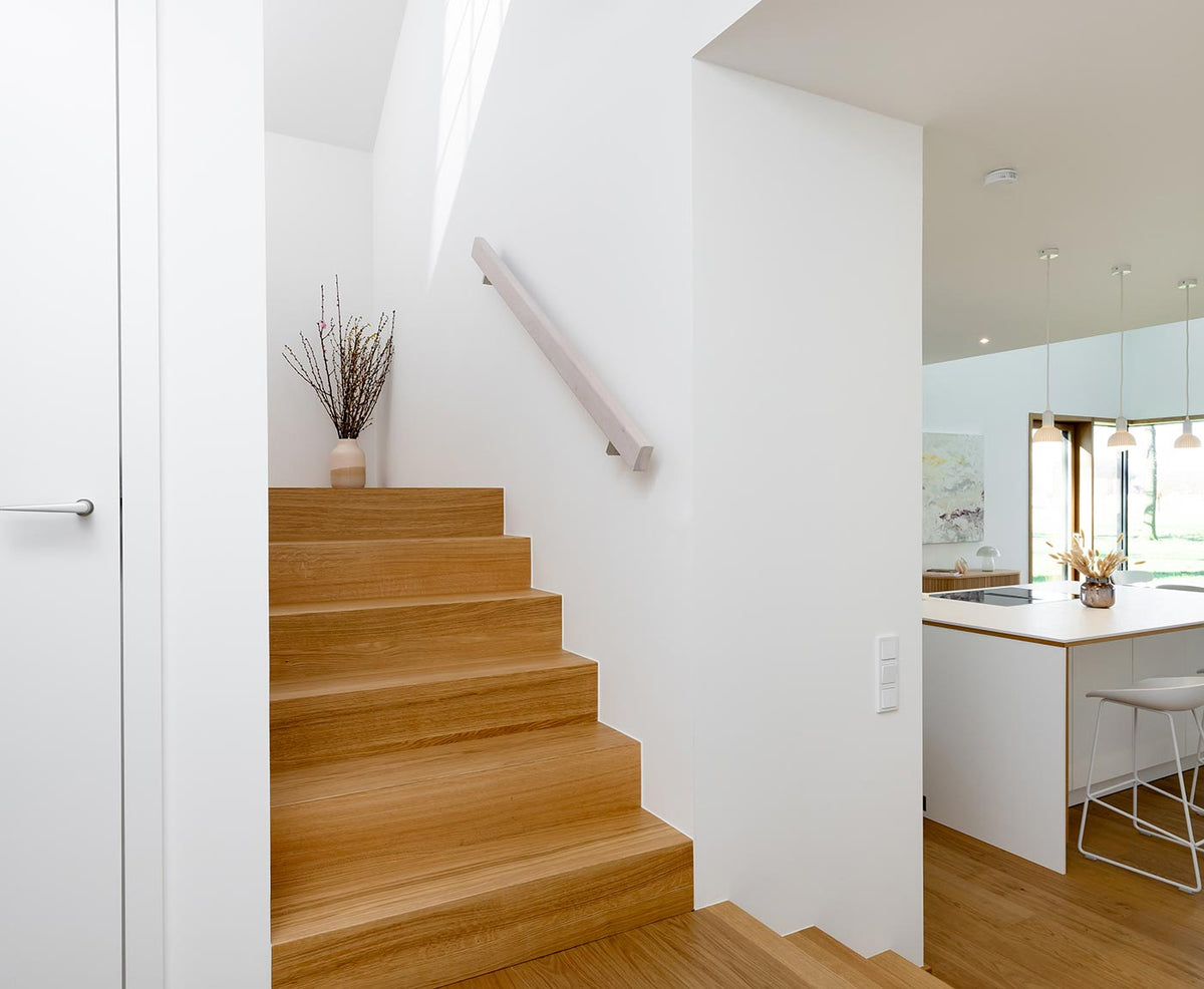 Treppenaufgang in moderner Wohnung mit rechteckigem Handlauf aus Holz in weiß.