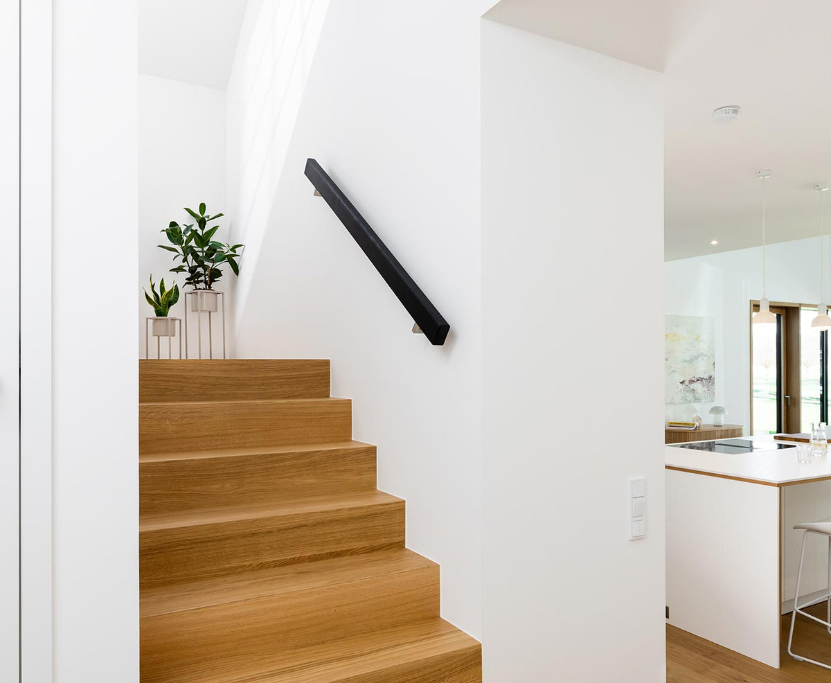 Moderne Wohnung mit Holztreppe und rechteckigem Handlauf Holz in schwarz an weißer Wand.