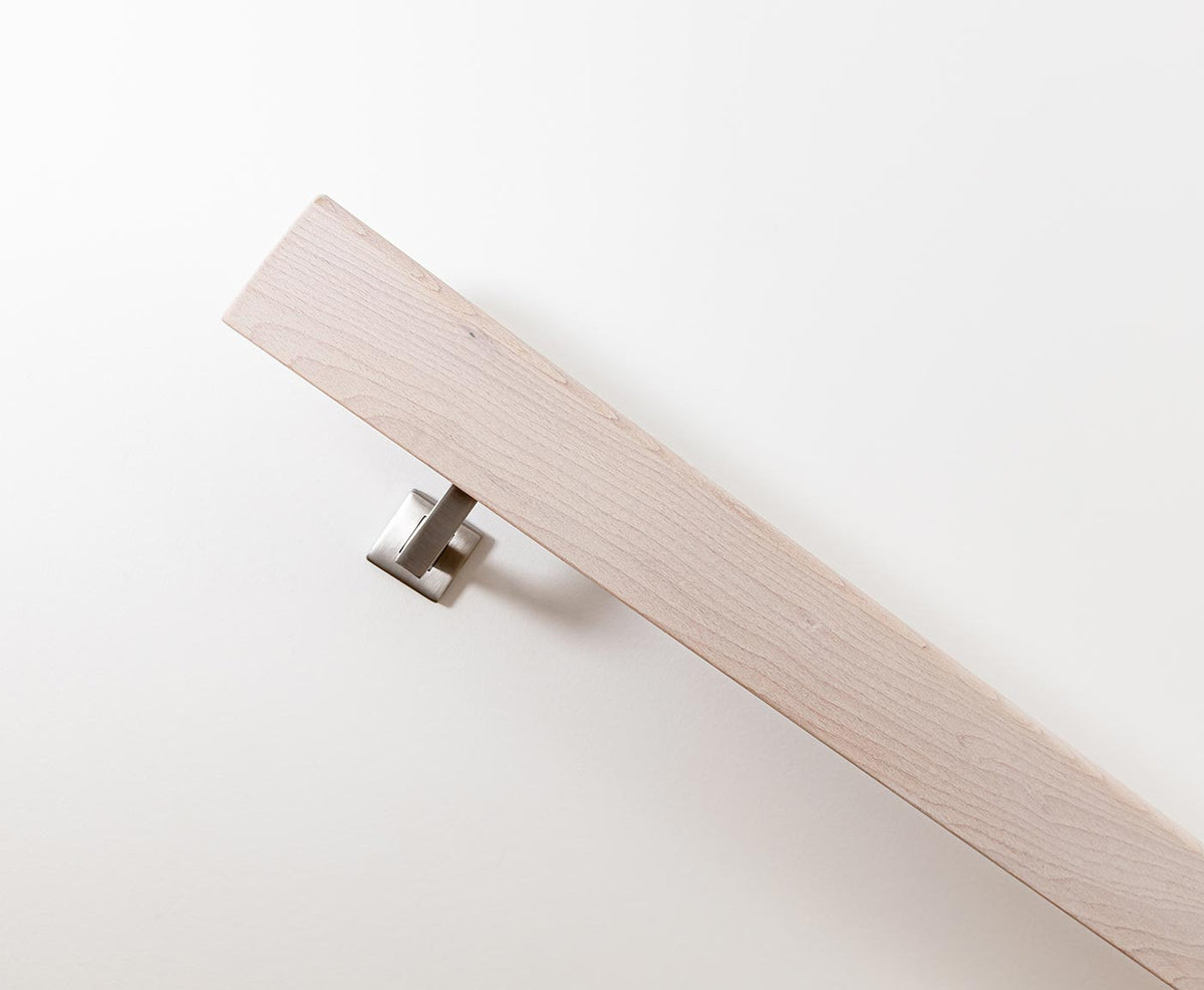 Seitliche Aufnahme eines Handlauf aus Holz im Farbton weiß, leicht deckend, mit modernem Halter.