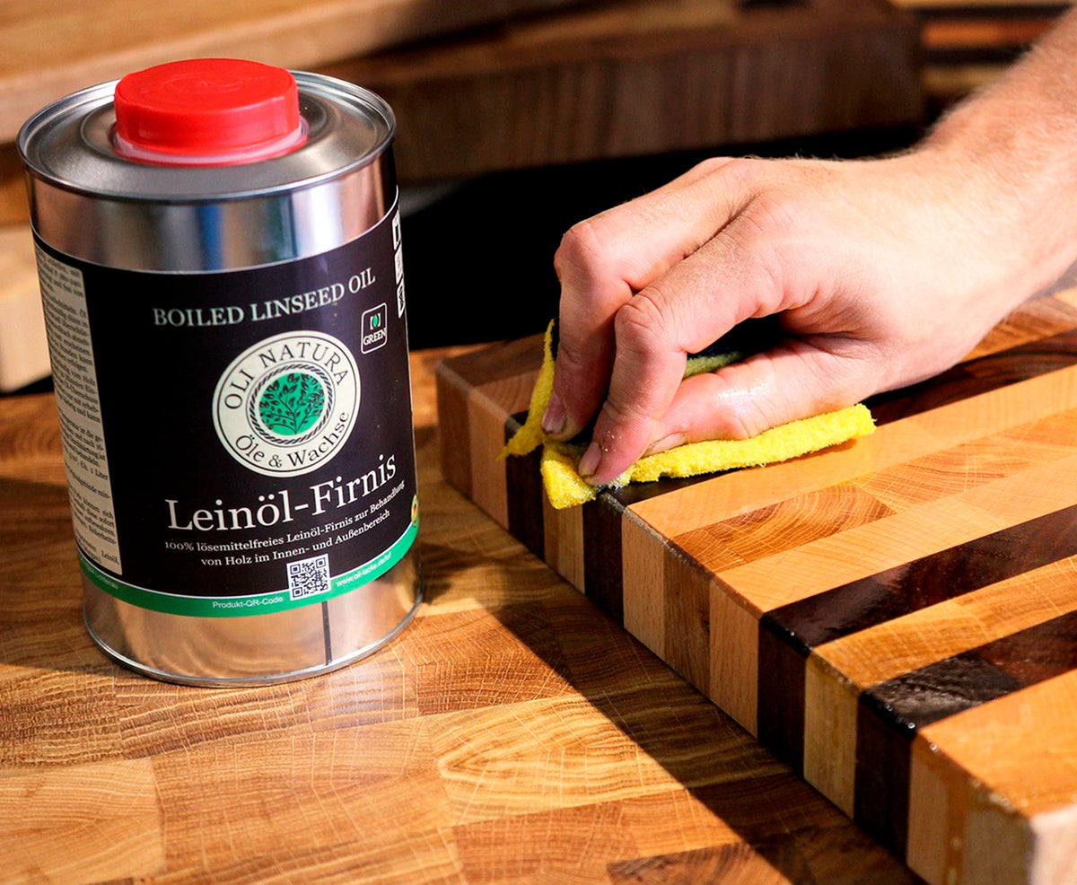 Hand mit gelbem Lappen die gestreiftes Holzbrett einölt, daneben Oli-Natura Leinöl-Firnis.